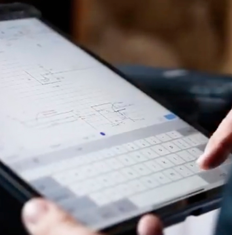 A close-up of a person using a tablet with a keyboard, displaying technical drawings or blueprints on the screen.
