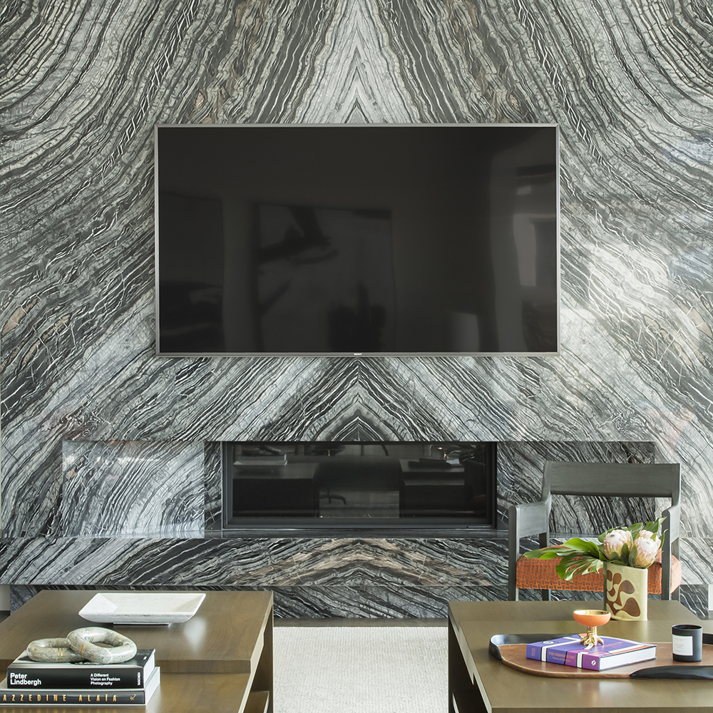 This image shows a stylish living room with a large TV mounted on a stunning feature wall made of veined black and white marble, complemented by modern wooden furniture and decor.