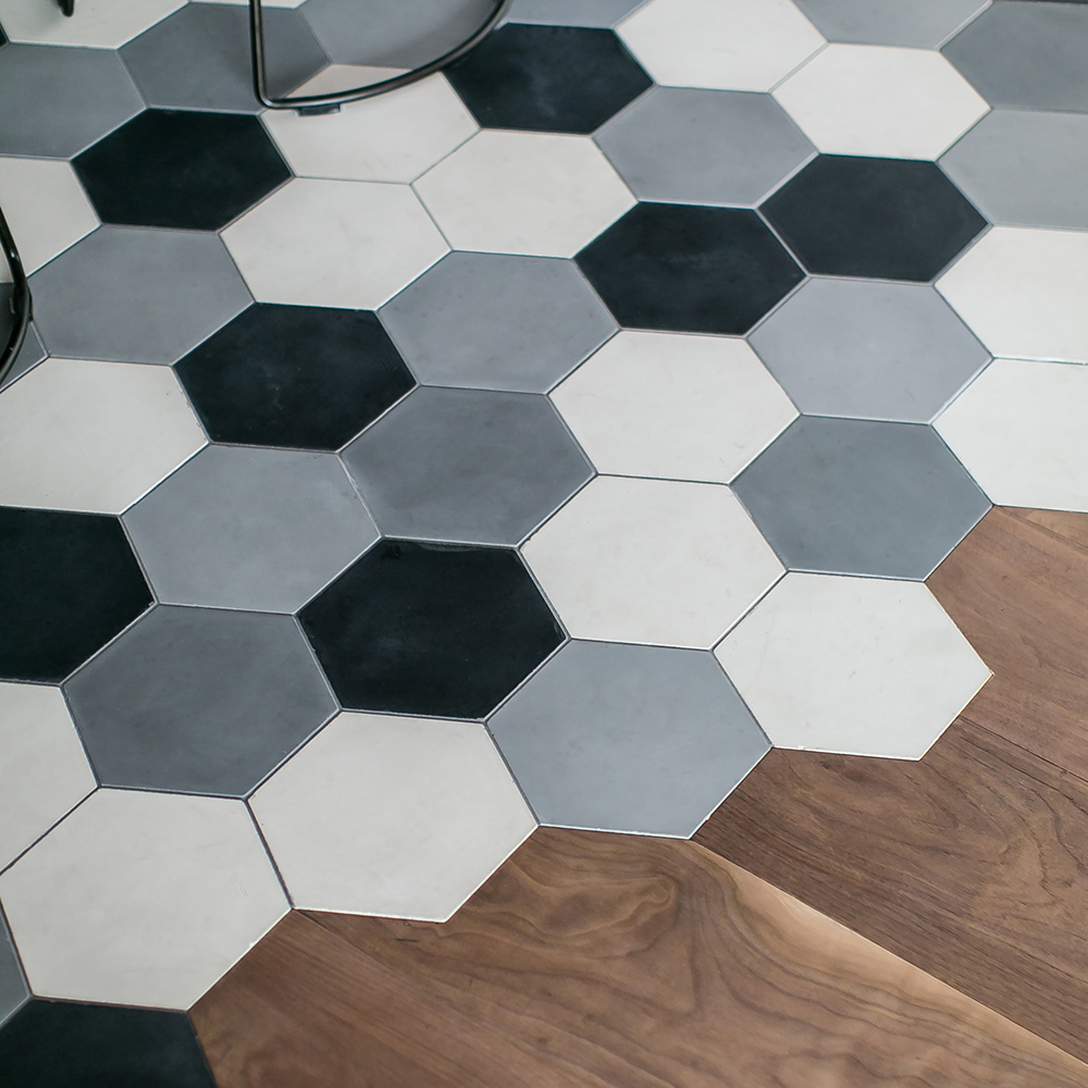 This image shows a section of flooring with hexagonal tiles in shades of black, gray, and white, transitioning into wood flooring with a distinct contrast.