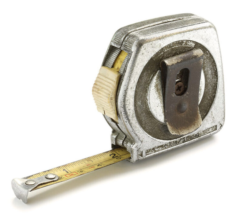 This image shows a vintage metal tape measure with a yellow tape extended, featuring a rusted clip and a worn appearance, indicating frequent use.