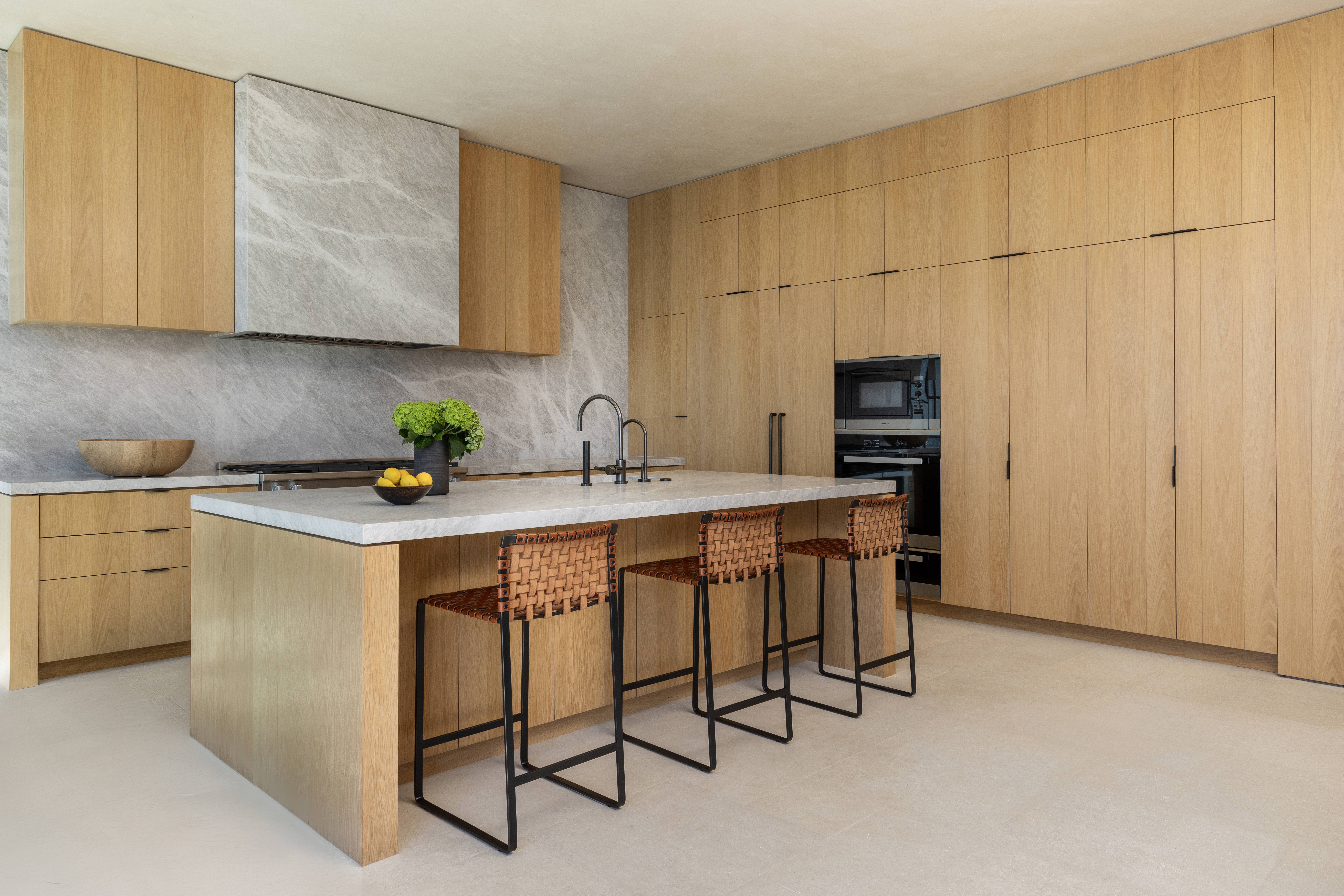 Modern custom kitchen with a spacious island, integrated seating, natural wood cabinetry, and a light stone countertop.