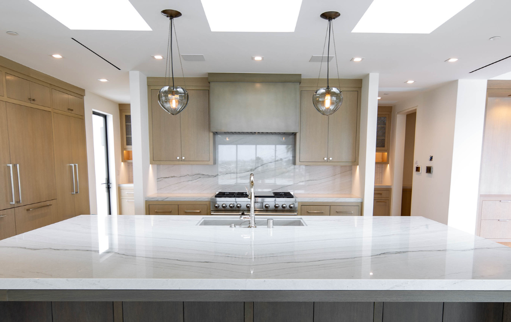Large kitchen island with a light natural stone countertop, waterfall edge, and custom cabinetry in a modern luxury kitchen.